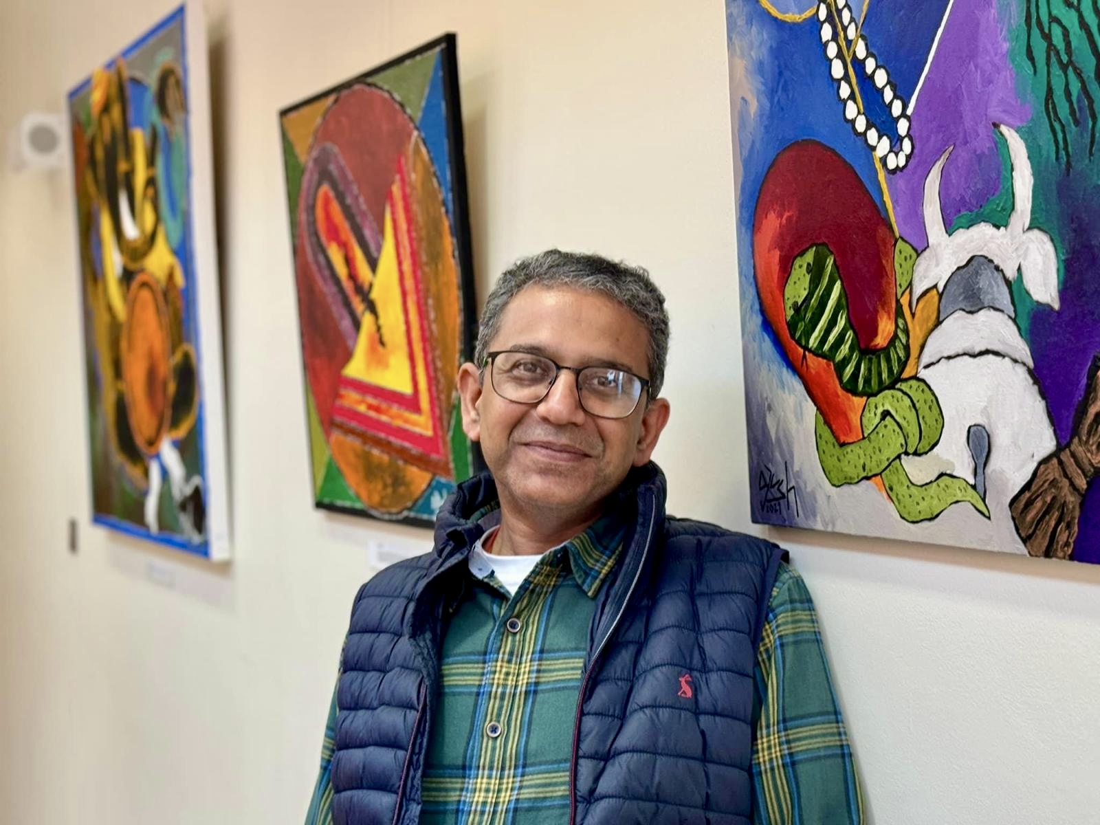 Artist Ayush Sinha standing beside his paintings at an exhibition.